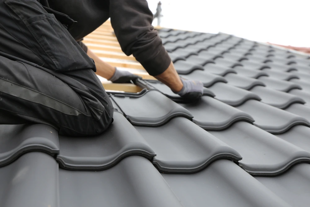 Ouvrier en tenue de travail noire installant des tuiles sur une toiture