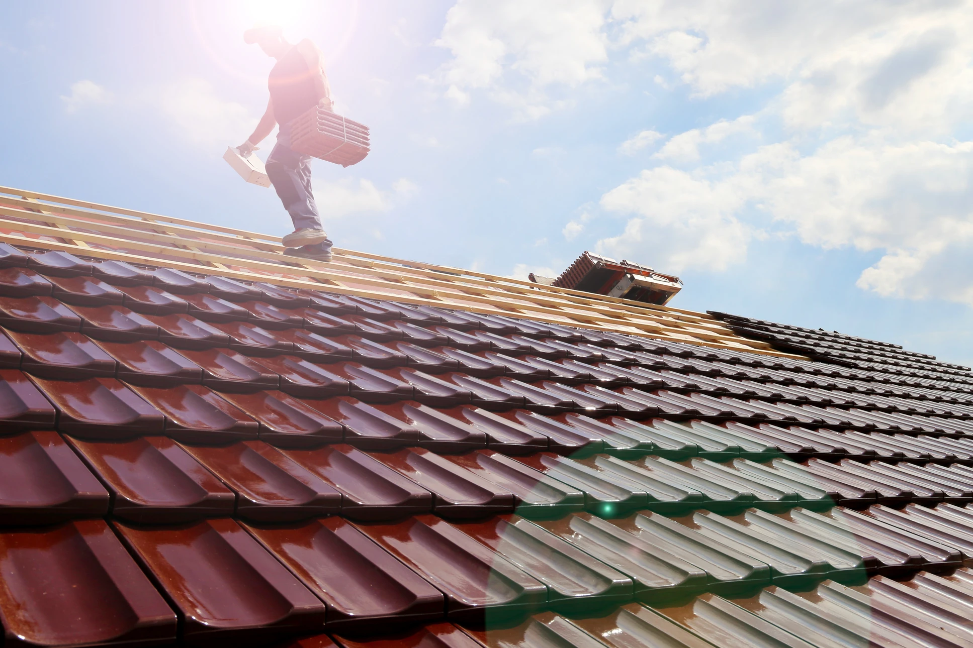 Ouvrier couvreur installant des tuiles sur une toiture en pente sous un ciel nuageux