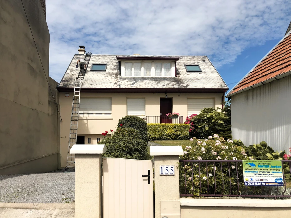 Technicien en couverture grimpant une échelle appuyée sur une maison pavillonnaire