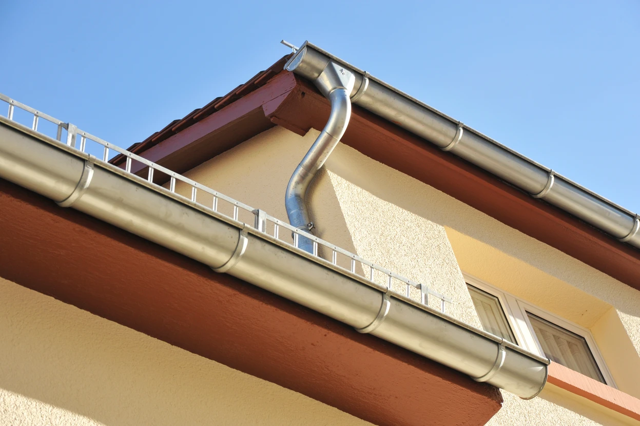 Chantier de construction résidentielle en extérieur, toiture en tuiles métalliques grises ondulées avec gouttière aluminium installée