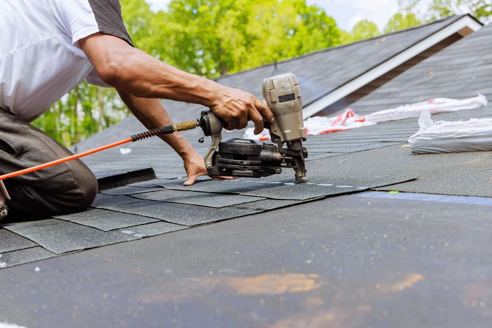Deux couvreurs professionnels travaillent sur une toiture en pente sous un ciel bleu