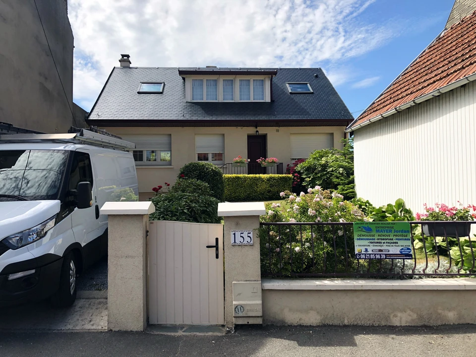 Couvreur professionnel travaillant sur toiture en tuiles métalliques, utilisant une échelle de toit pour accéder à une cheminée en briques